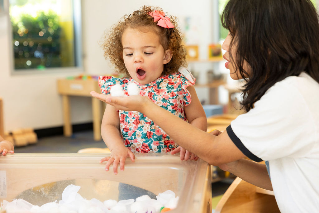Child blowing cotton balls with teacher at E3 School