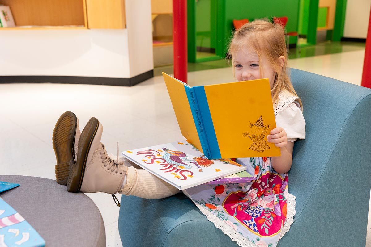Child reading a book with her feet propped up on a table at E3 School