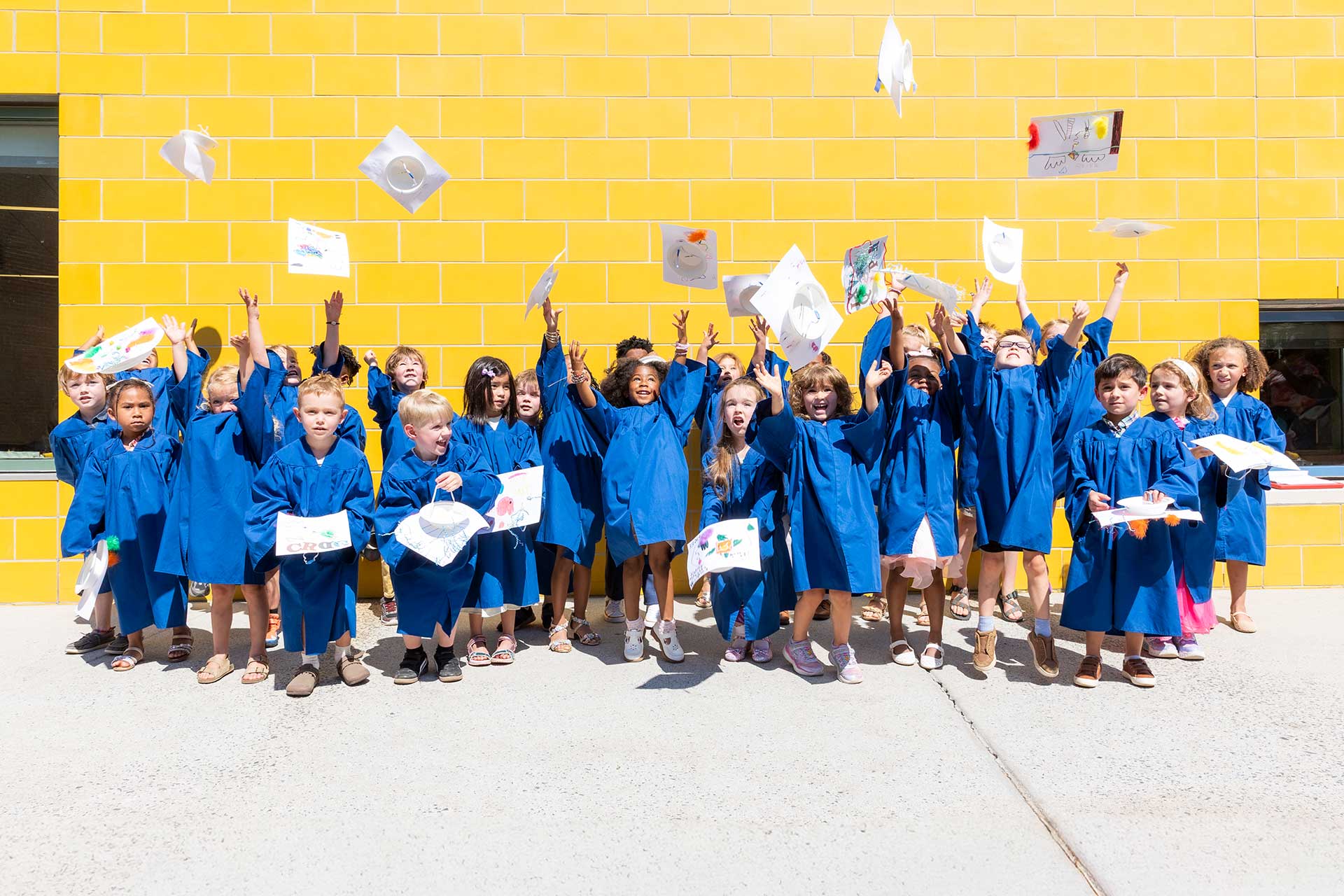 E3 school children in graduation gowns joyfully holding their diplomas, celebrating their academic achievements together.